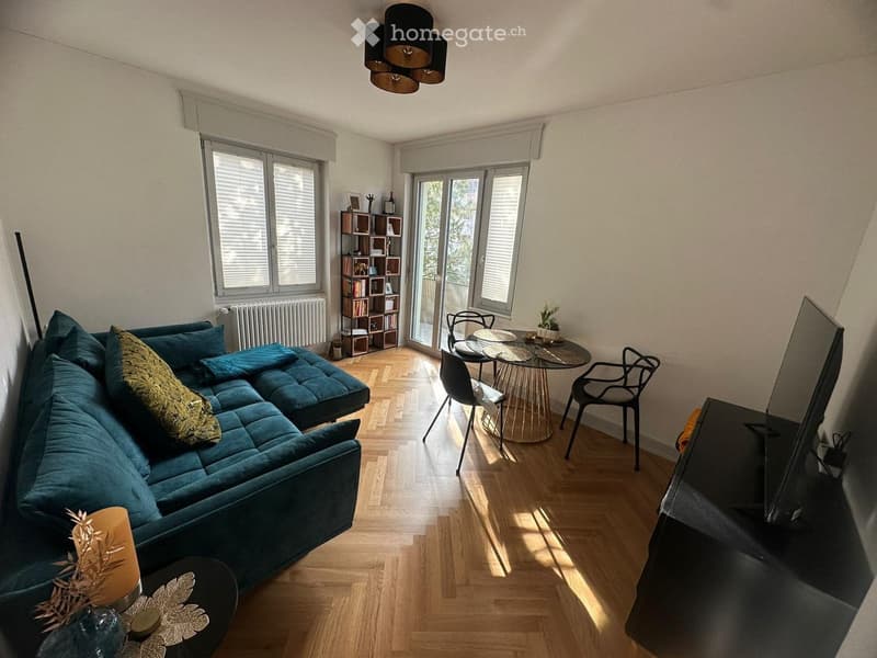Modern living room with a teal sectional sofa, coffee table, dining area with chairs and table, bookshelf, and TV stand.