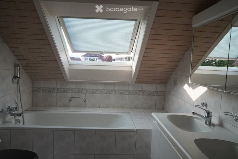 Modern bathroom with a skylight window, wooden ceiling, tiled walls, bathtub, sink, and mirror.
