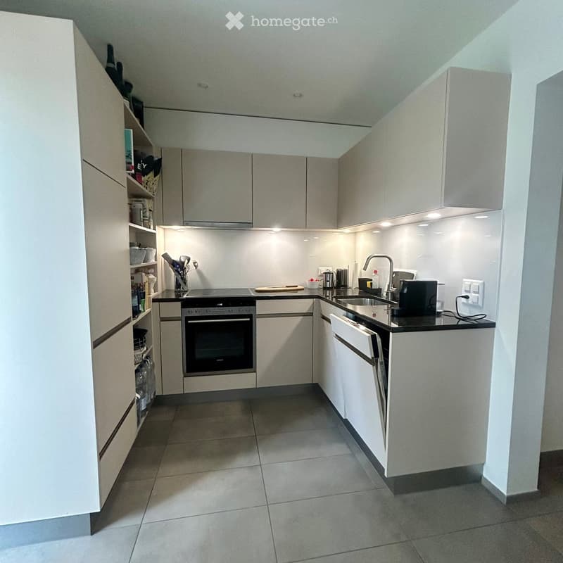 Modern kitchen with white cabinets, black countertops, and stainless steel appliances including an oven, sink, and toaster. The space features built-in storage and a sleek, contemporary design.