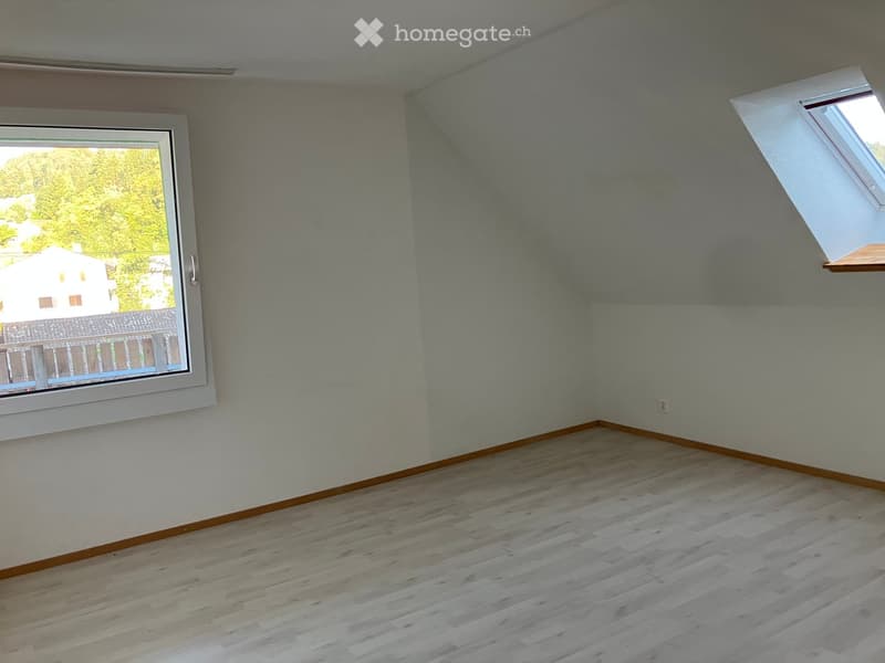 Empty room with light grey walls, wooden flooring, and large windows with white frames. One window has a small skylight above it.