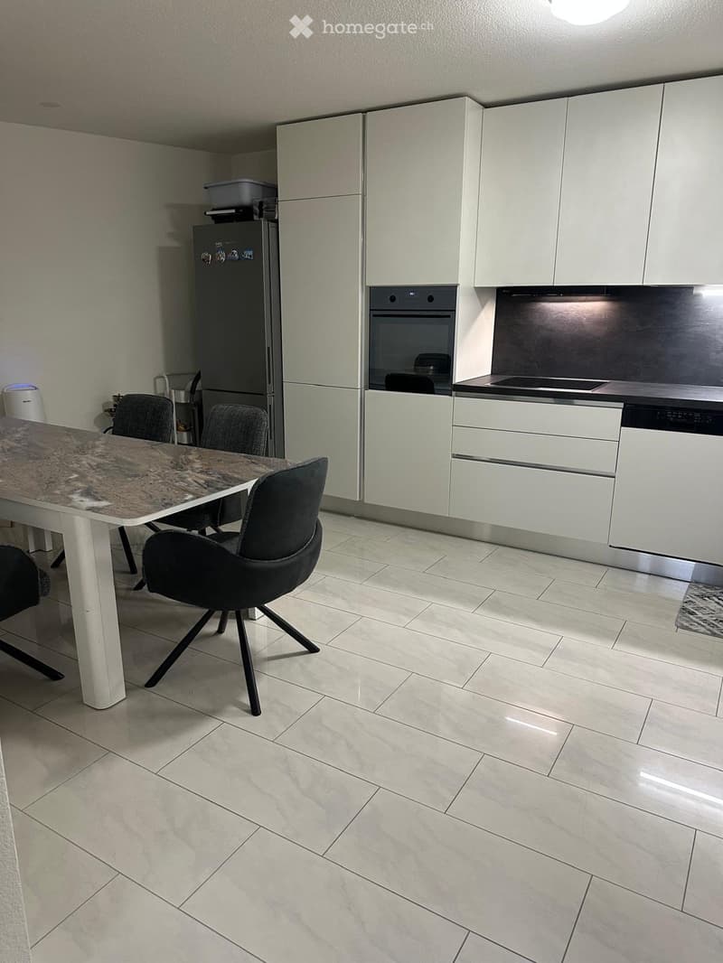 Modern kitchen with white cabinets, stainless steel appliances, a dining table with chairs, and tiled flooring.