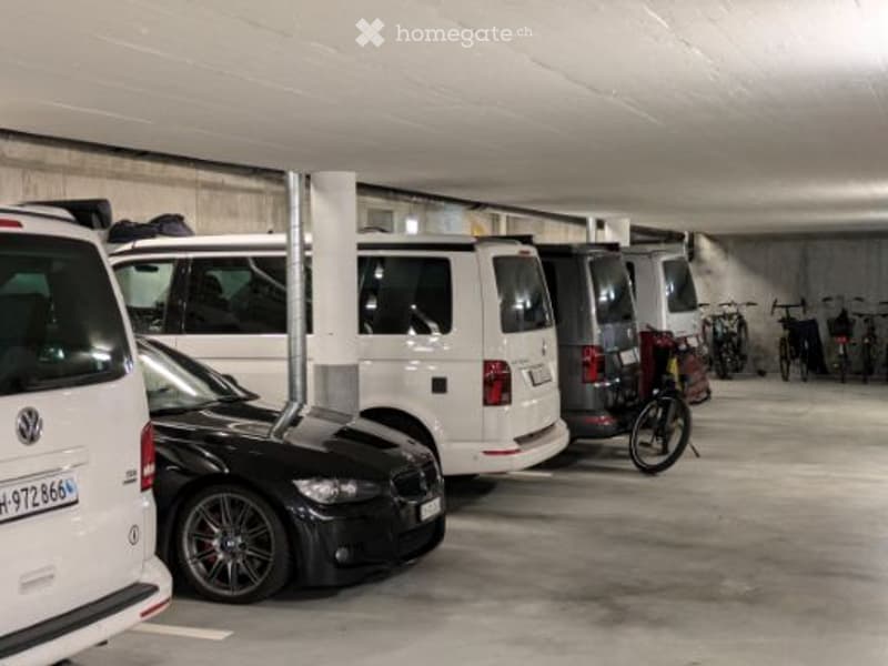 Underground parking area with several parked cars and bicycles, concrete walls and ceiling, organized parking spaces.