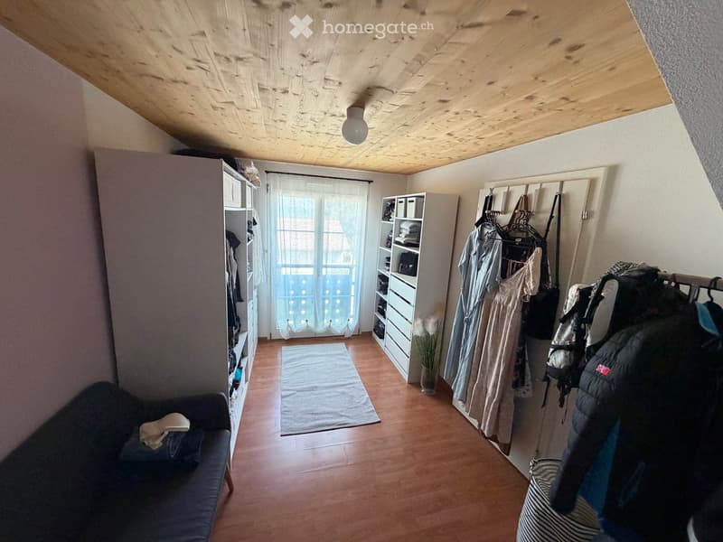 A small, furnished room with wooden flooring, a sofa, a shelf, a coat rack, and a small rug.