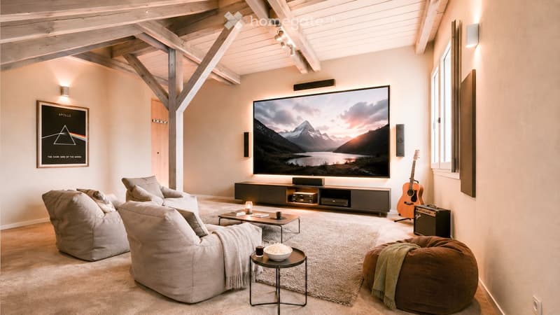 Modern living room with exposed wooden beams, large screen, comfortable seating, coffee table, and decorative items.