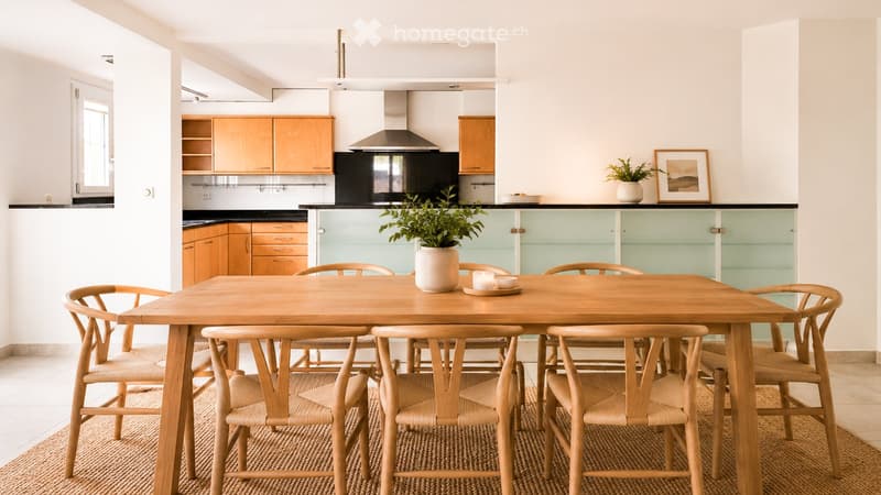 Bright kitchen with wooden cabinets, a central dining table with six chairs, a range hood, and a potted plant on the counter.