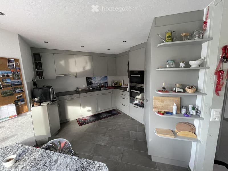 Modern kitchen with grey cabinets, stainless steel appliances, granite countertop, and open shelving with various kitchen items.