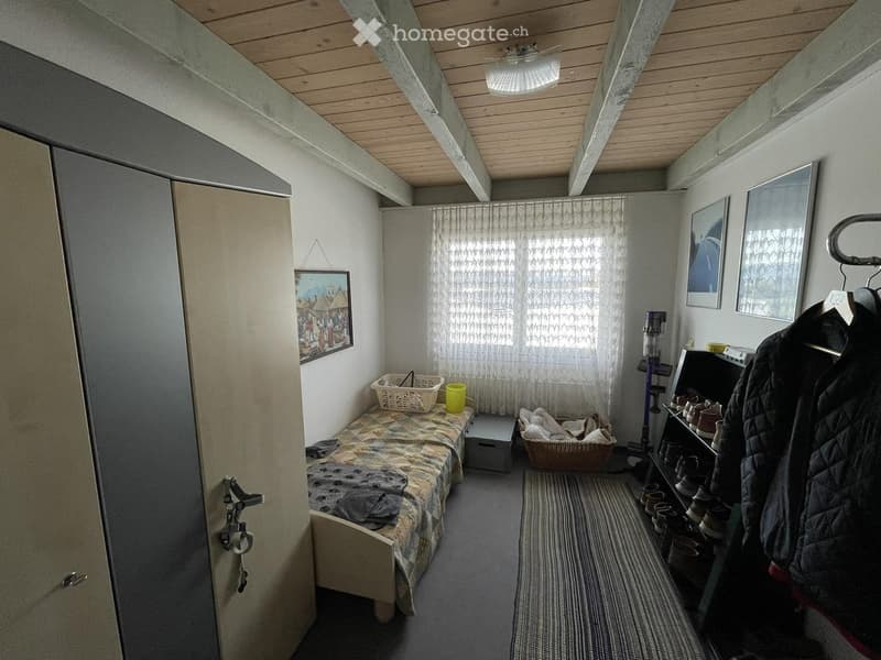 Small bedroom with a single bed, wardrobe, basket, cup, stool, picture frame, shoe rack, and coat hanging on the wall.