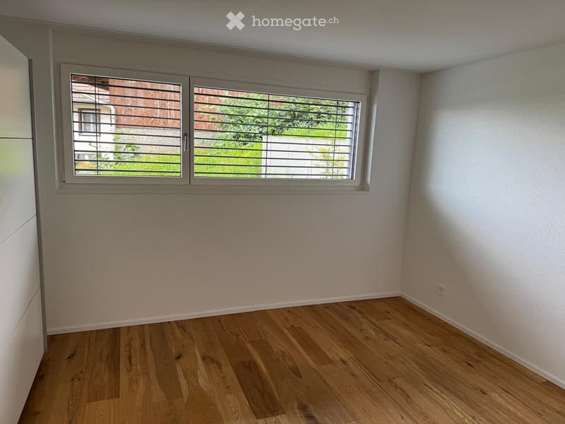 Empty room with light wooden flooring, white walls, and large windows with blinds. No furniture or equipment present.