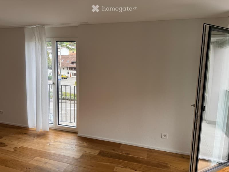 Empty room with wooden flooring, large sliding glass doors leading to a balcony, and white walls.