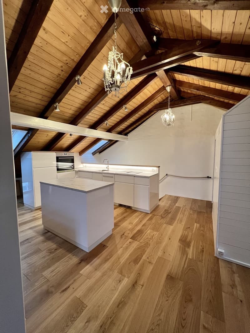 Modern kitchen with white cabinets, a central island, and wooden flooring. Exposed wooden beams and a chandelier adorn the vaulted ceiling.