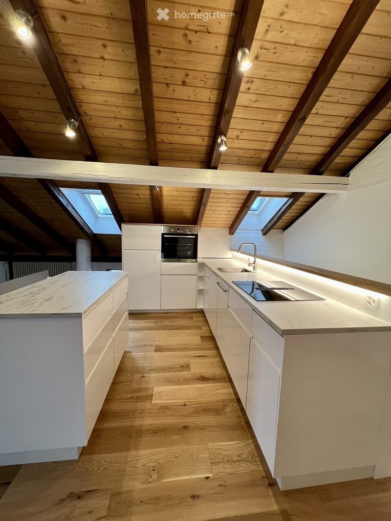 Modern kitchen with white cabinets, wooden flooring, marble countertop, stainless steel sink, and built-in oven. Features skylight windows and recessed lighting.