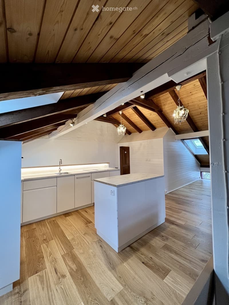 Modern kitchen with white cabinets, a central island, and wooden flooring. Features a sink with a faucet, built-in lighting, and exposed wooden beams on the ceiling.