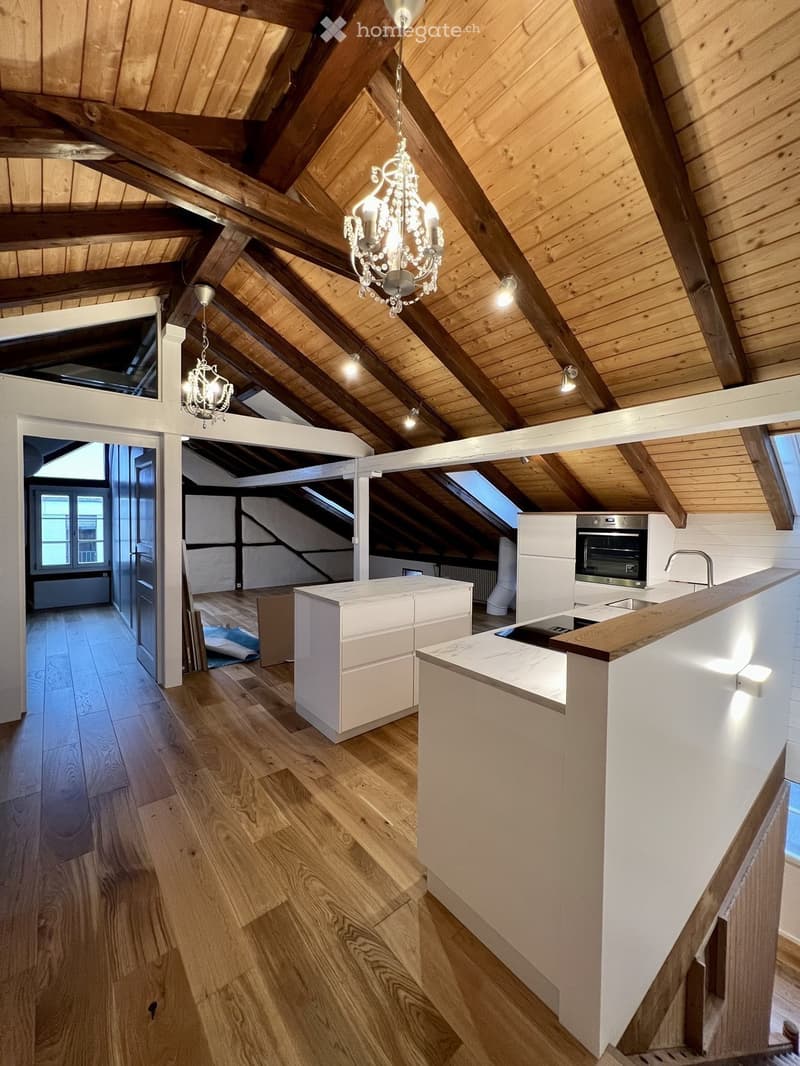 Modern kitchen with wooden floors, white cabinets, a central island, and exposed wooden beams on the ceiling.