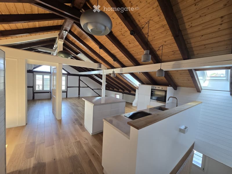 Modern kitchen with wooden floors, white cabinets, central island, and hanging pendant lights.