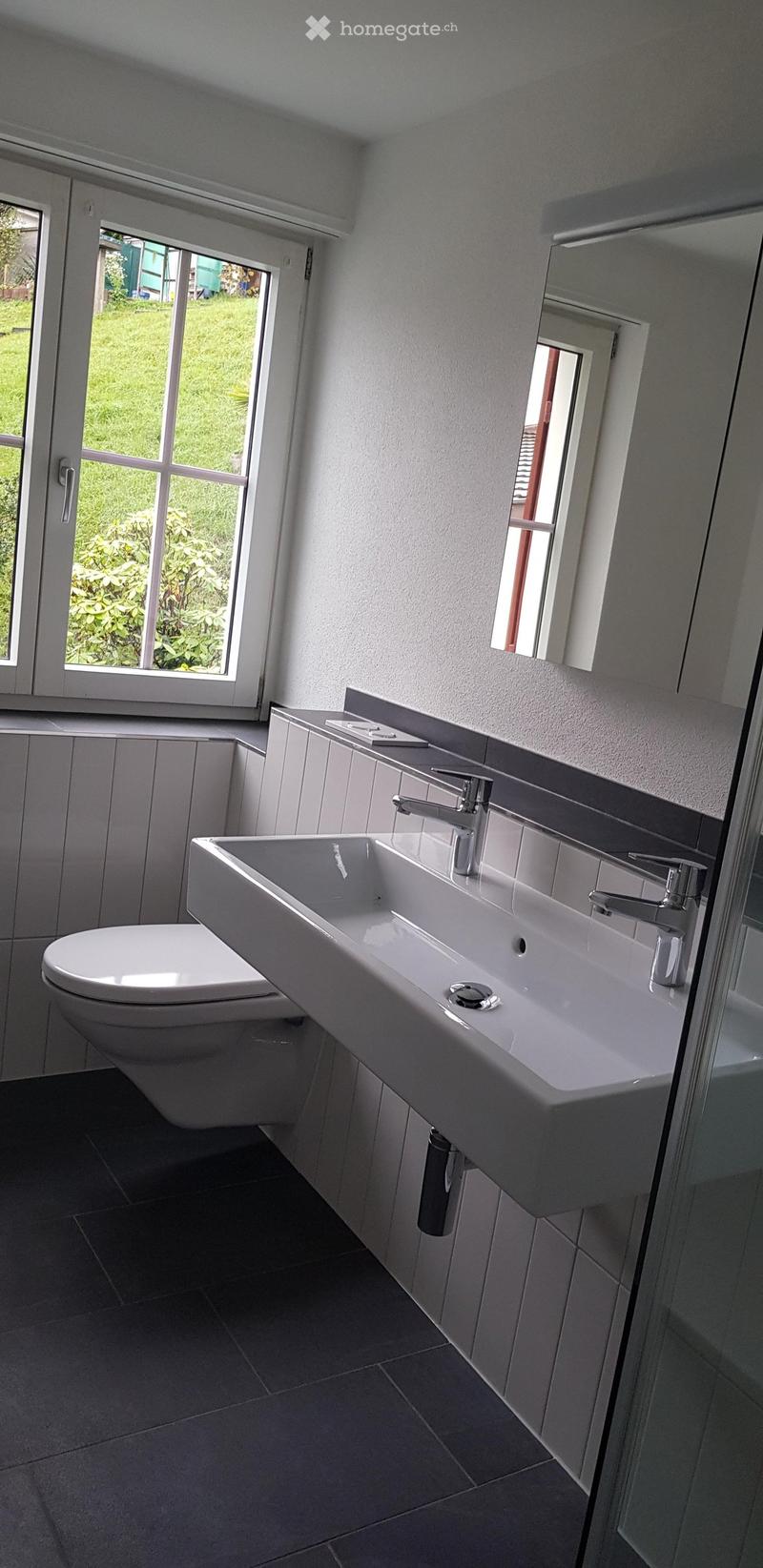 Modern bathroom with a white sink, chrome faucet, and large windows offering a view of the garden.
