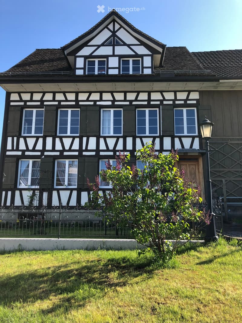 Traditional style house, two stories, brown roof, white and black facade, many windows, black fence in front, green lawn