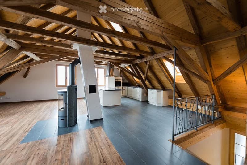 Attic room with wooden beams, gray tiled floor, white cabinetry, integrated fireplace, and black railings.