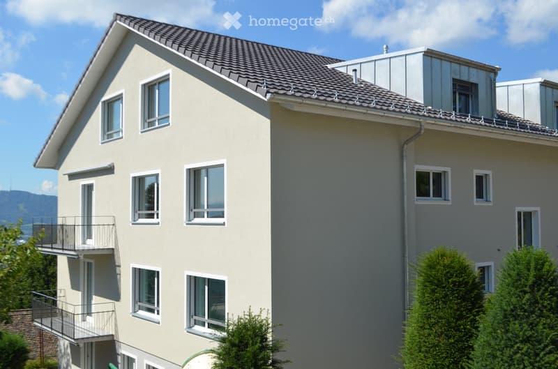 Two-story house with beige exterior, multiple windows, and balconies on the upper level.