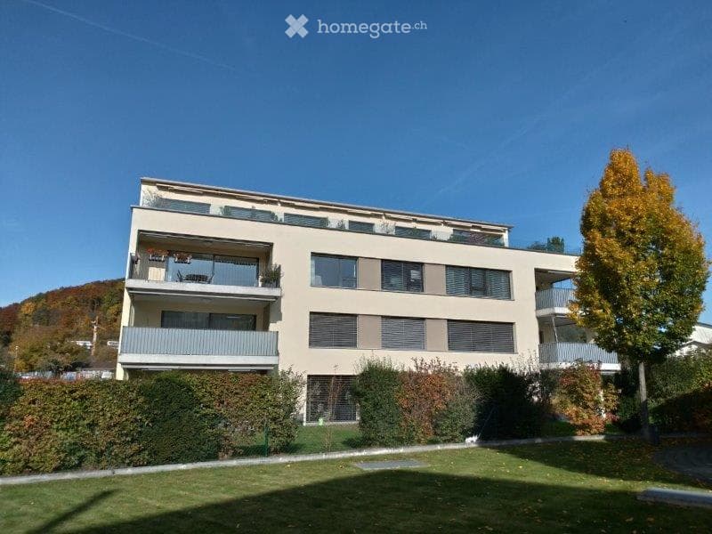 Modern multi-story apartment building with balconies, large windows, and surrounding greenery.