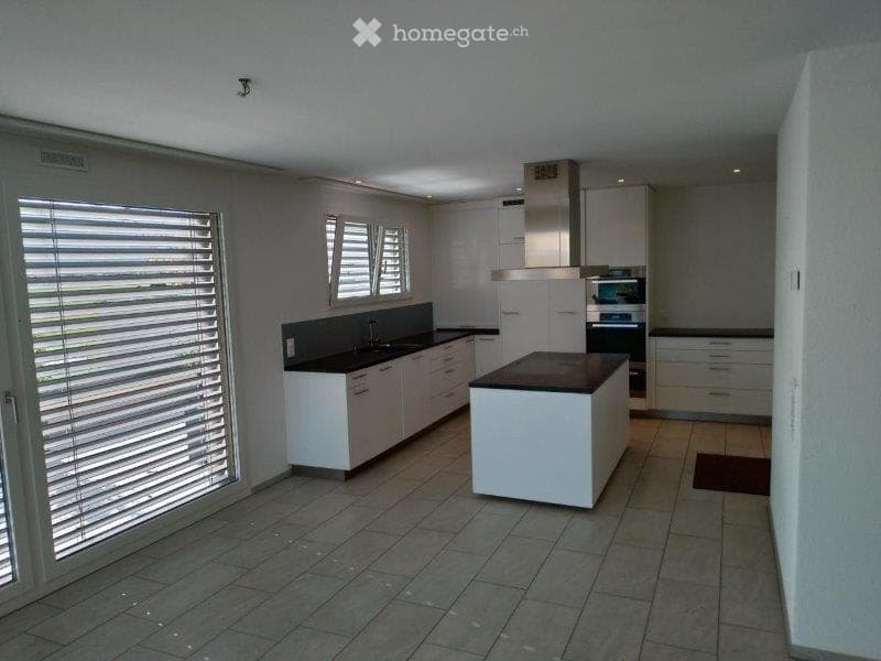 Modern kitchen with white cabinets, black countertops, and a central island. Features include a sink with a faucet, an oven, and a range hood.