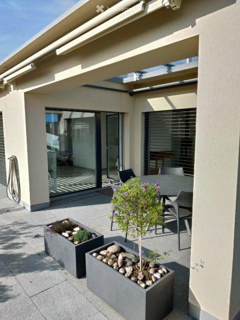 Modern patio with a covered roof, outdoor dining table and chairs, potted plants, and decorative planters with rocks.