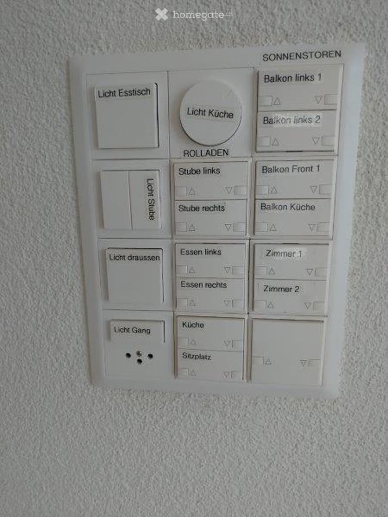 A modern light switch panel mounted on a white wall, featuring multiple buttons and a central rotary knob for controlling various lights and blinds in different rooms and balconies.