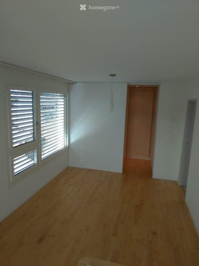 Empty room with wooden flooring, white walls, and large windows with blinds. No furniture or equipment present.