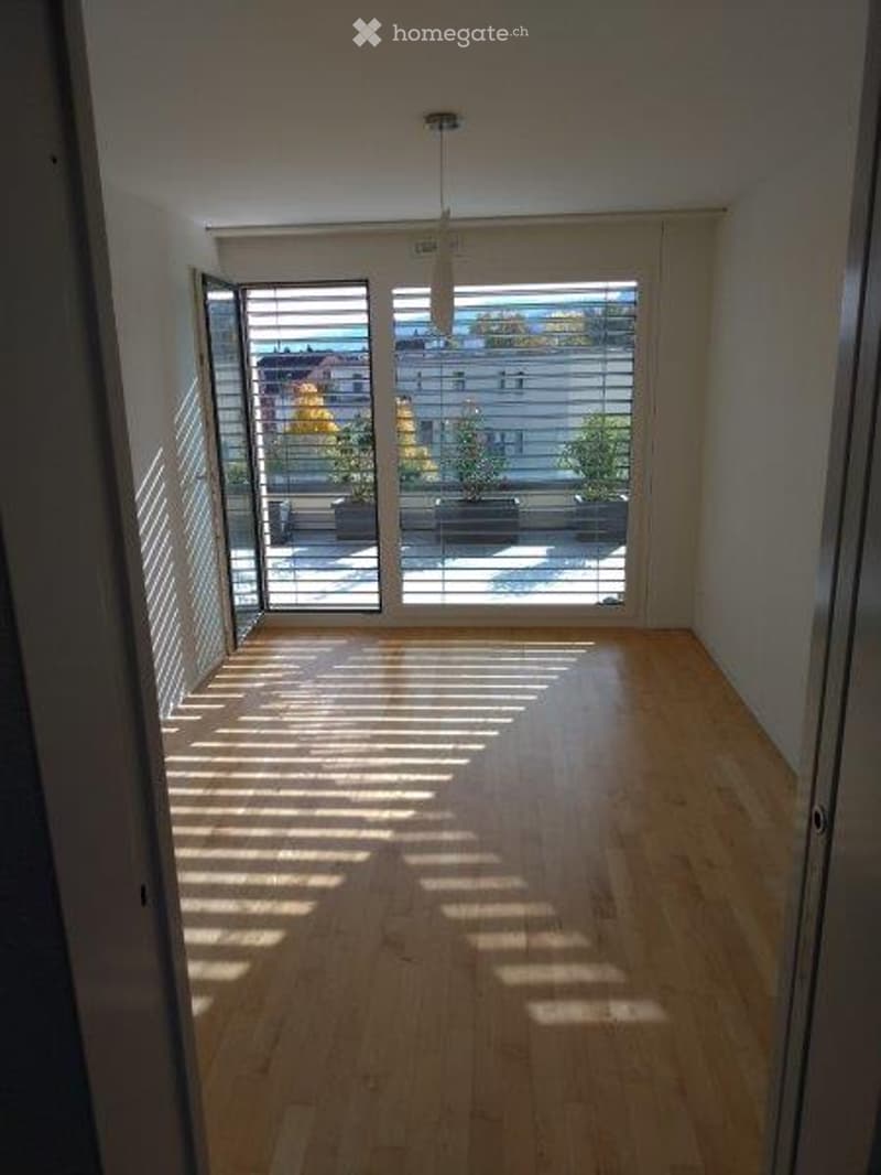 Empty room with wooden flooring, large windows, and a view of a balcony area with outdoor furniture.