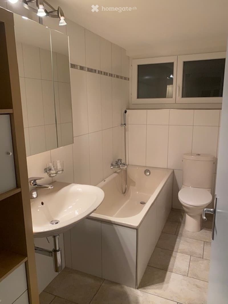 Modern bathroom with white tiles, a bathtub, toilet, sink, and a large mirror above the sink.