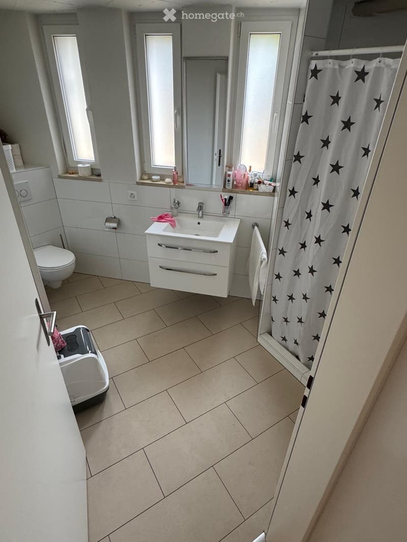 Modern bathroom with white tiles, a sink with a mirror, a toilet, a shower with a star-patterned curtain, and a towel hanging on the side.