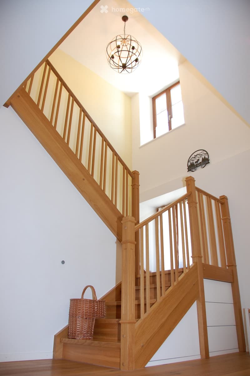 Wooden staircase with a modern chandelier, a wicker basket on the steps, and a decorative sign on the wall.