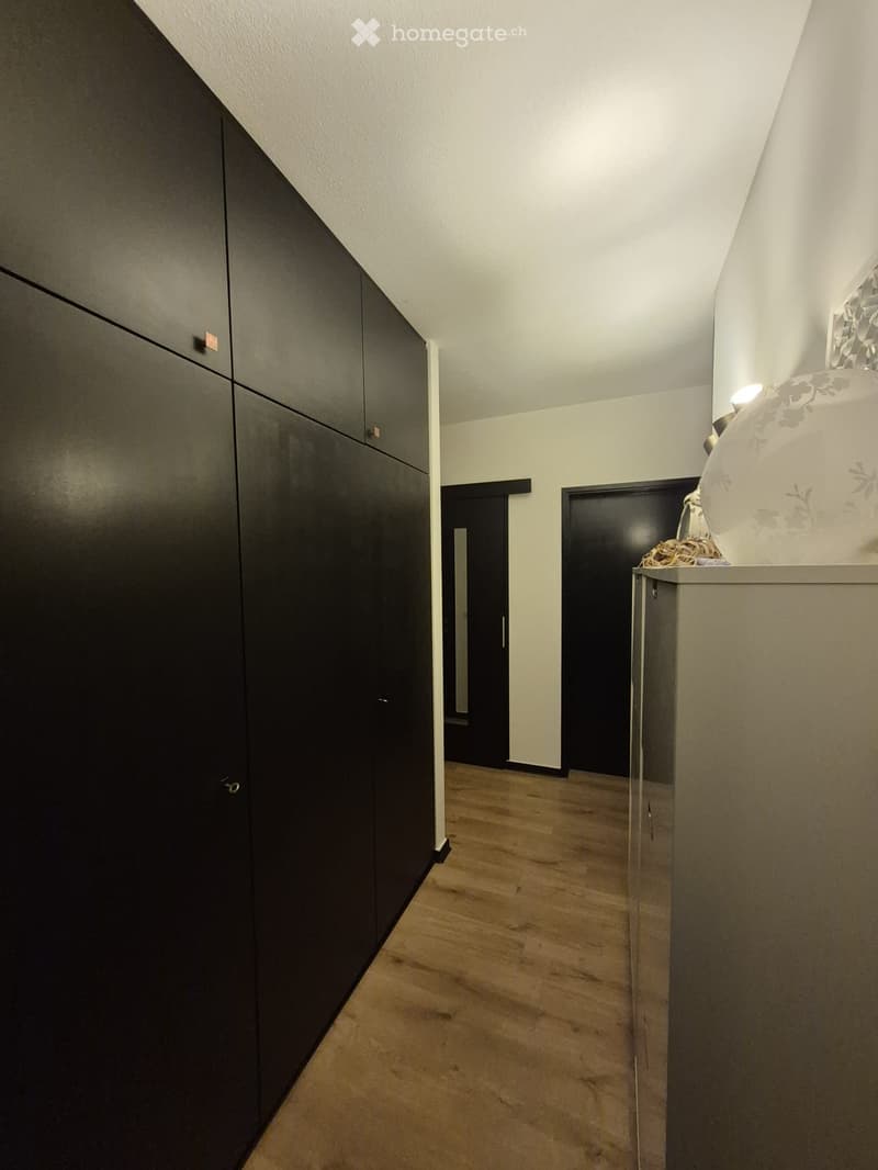 Modern hallway with wooden flooring, black cabinetry on one side, and a decorative vase on a small table on the right.