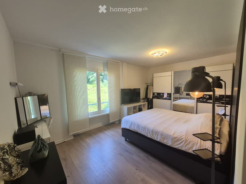 Modern bedroom with a large bed, nightstand, mirror, lamp, television, wardrobe, and a small table with a bag on it.