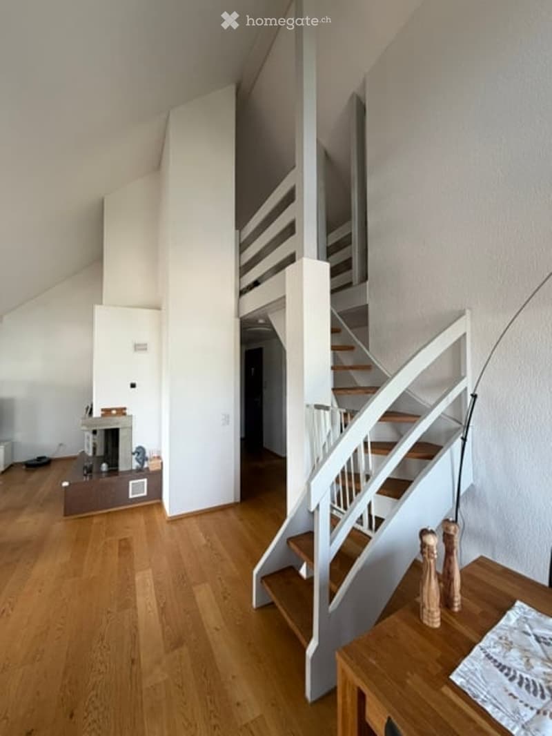 Modern, open-plan living space with wooden flooring, a curved staircase leading to an upper level, and a fireplace in the corner.