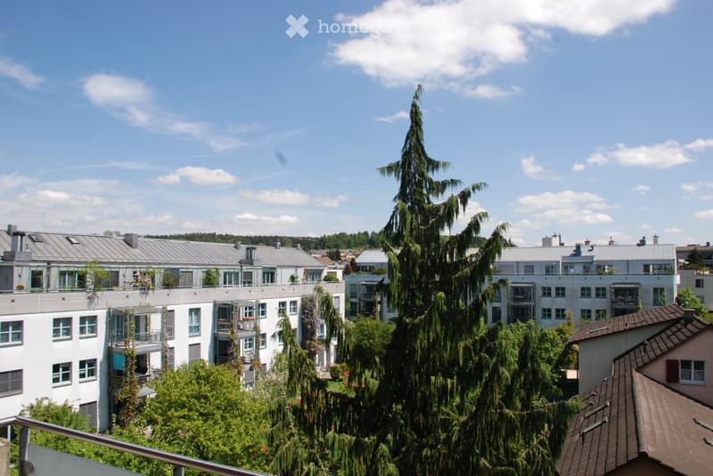 A multi-story residential building with modern architecture, featuring balconies, large windows, and surrounding greenery.