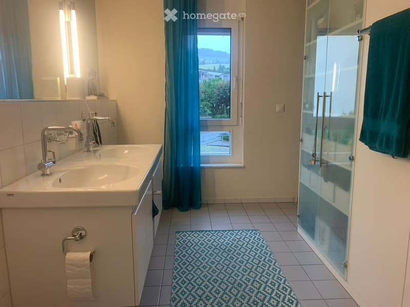 tiled floor, double sink, window with turquoise curtain, glass shower, towel rack