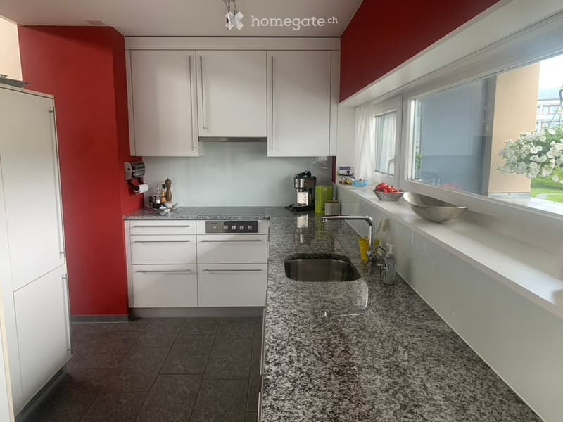 modern kitchen with granite countertops, stainless steel sink, built-in appliances, white cabinetry, red accent wall, large windows, and a view of the outside