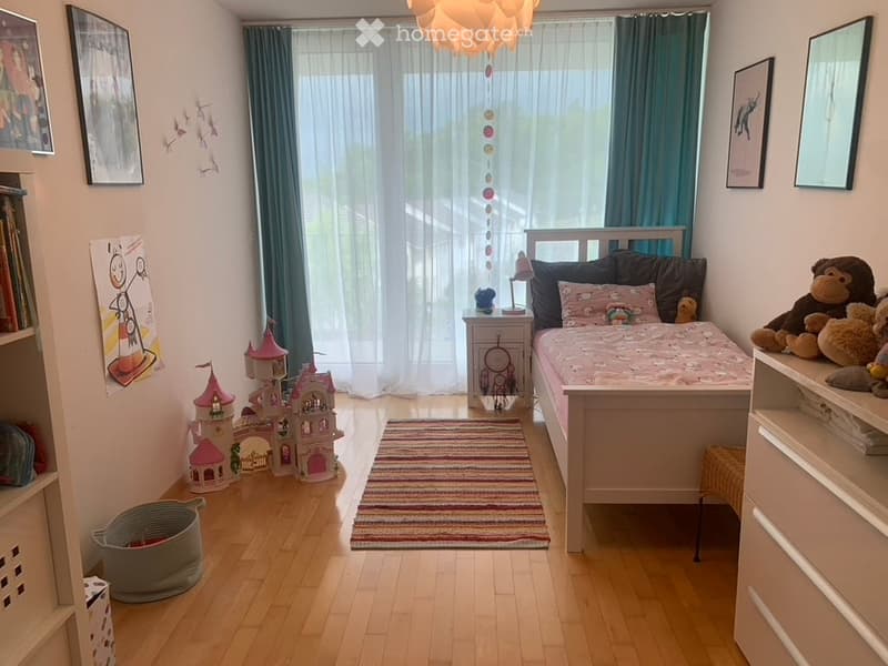 bedroom with bed, rug, toy castle, bookshelves, storage basket, wall pictures, white curtains