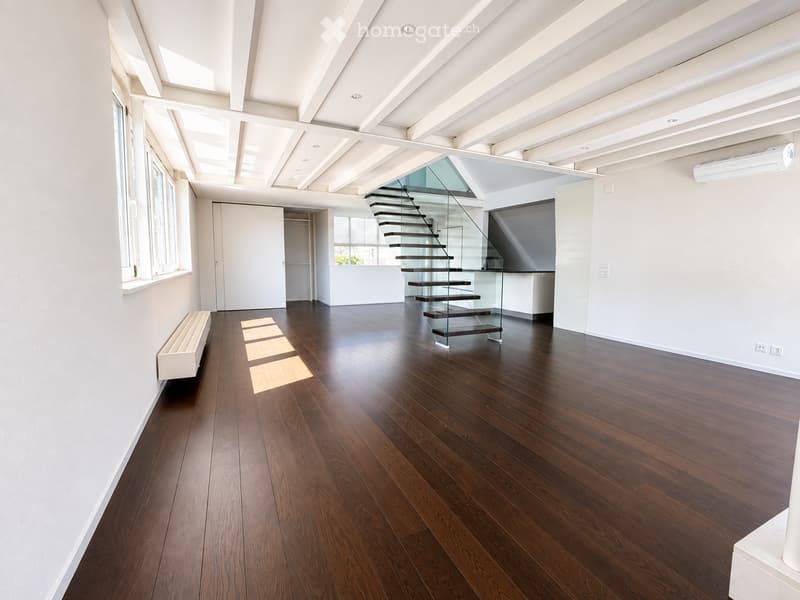 Empty room with dark hardwood flooring, white walls, large windows, and a modern glass staircase leading upwards.