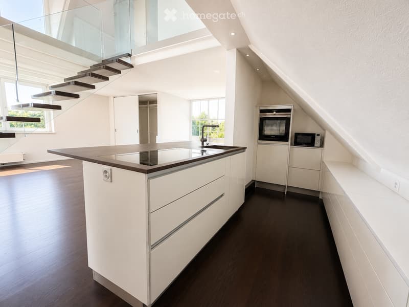 Modern kitchen with white cabinets, dark wooden floor, central island with sink and faucet, built-in oven and microwave, and large windows providing natural light.