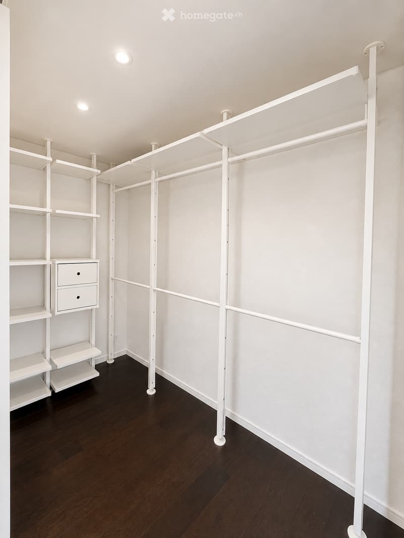 Empty closet with white shelving units, dark hardwood flooring, and recessed lighting.
