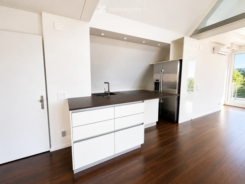 Modern kitchen with white cabinets, dark countertop, stainless steel sink and faucet, and a stainless steel refrigerator. The floor is made of polished wood.