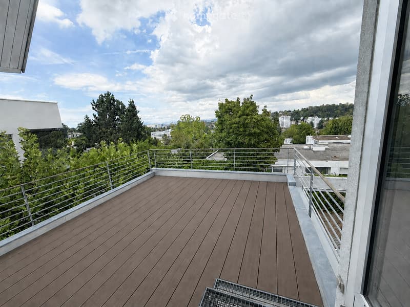 Wooden deck with metal railing, overlooking a cityscape with trees and buildings.