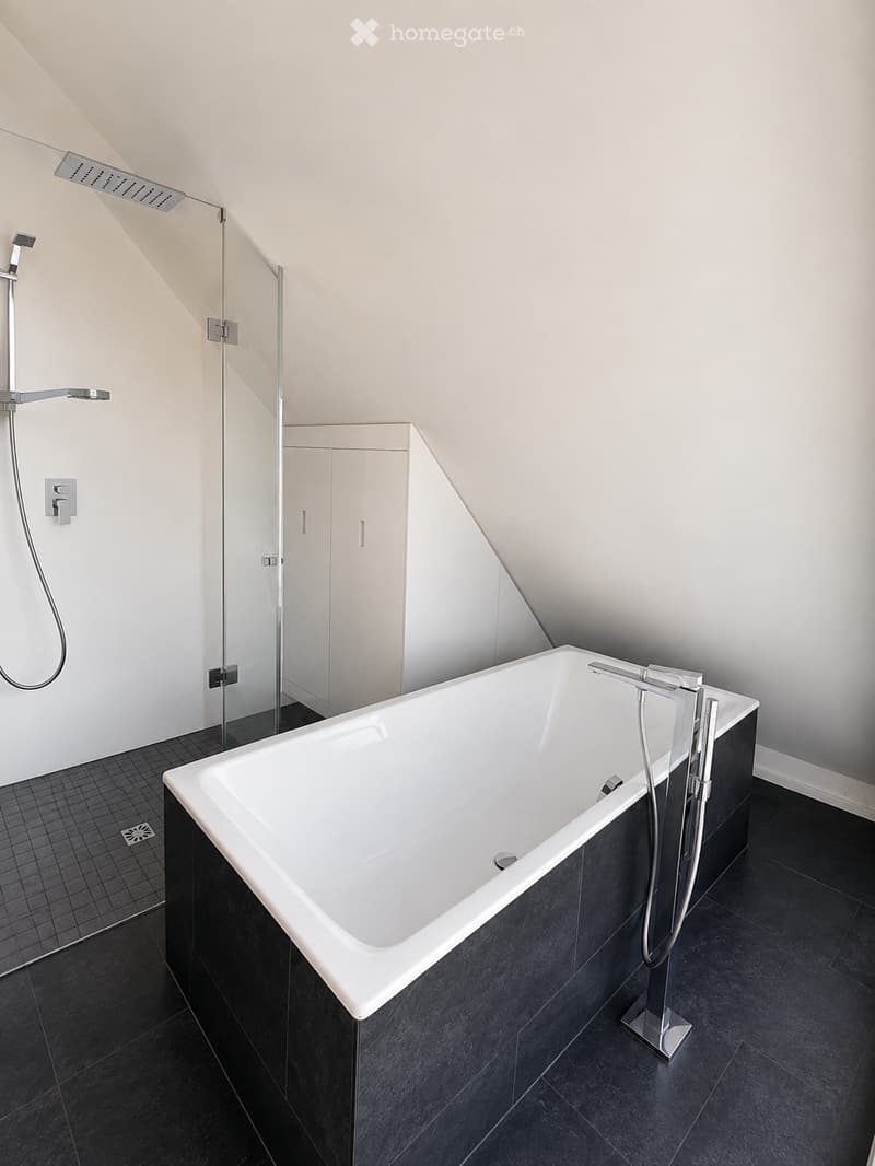 Modern bathroom with a white bathtub, sleek black tiles, a glass shower enclosure, and a modern faucet system.