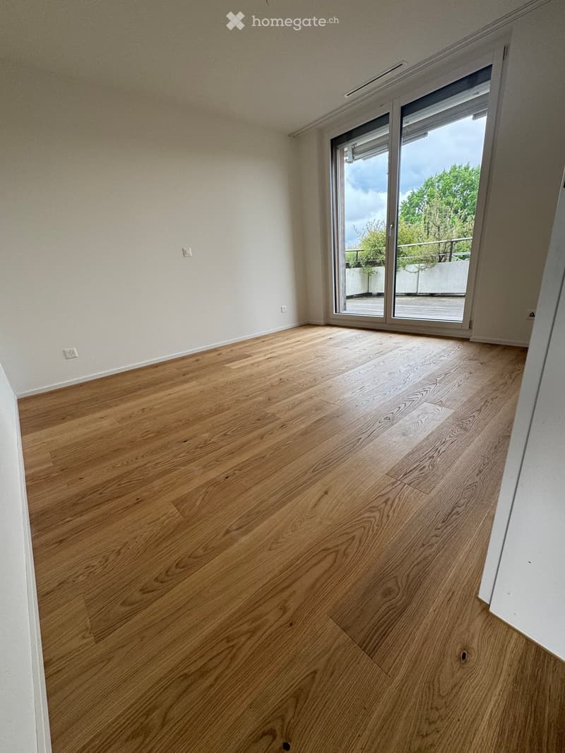 Empty room with wooden flooring and white walls, featuring a large sliding glass door leading to a balcony.