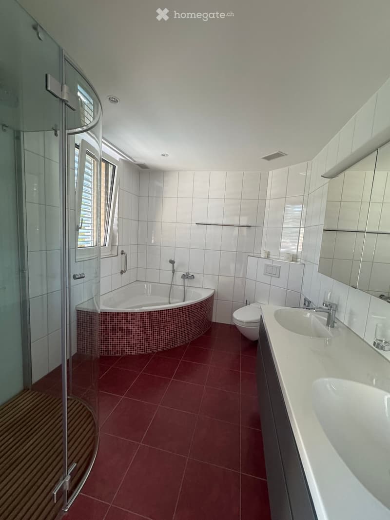 Modern bathroom with red tiled floor, white tiled walls, a corner bathtub, a toilet, a double sink vanity, and a glass-enclosed shower stall.