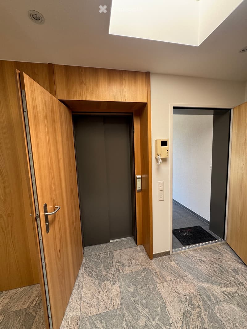 Modern hallway with marble flooring, wooden panel walls, and an intercom system mounted on the wall.