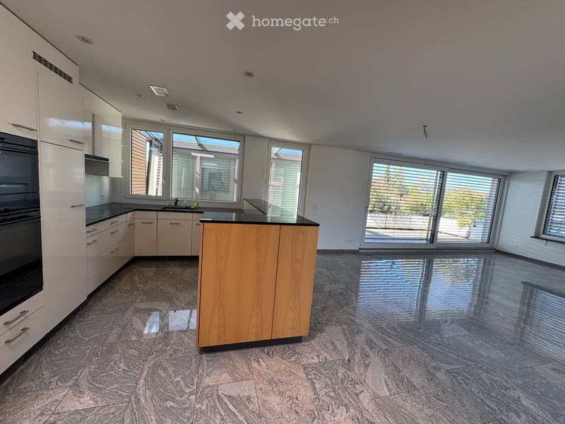 Modern kitchen with light-colored cabinets, a central island, and large windows offering a view of the outdoors.
