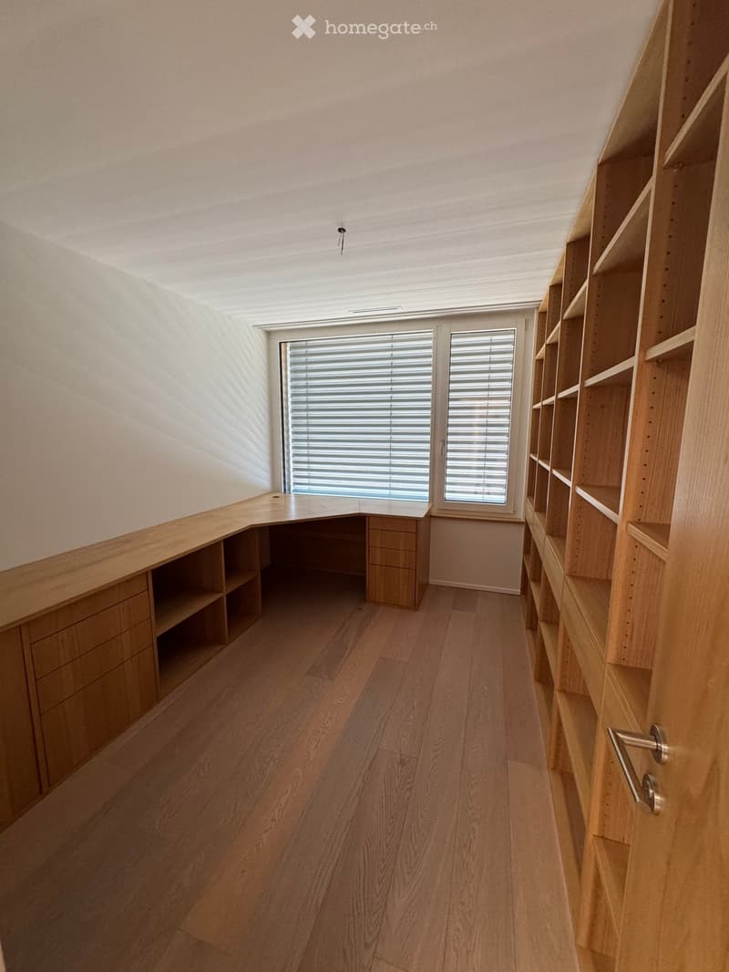 Empty room with wooden flooring, built-in wooden shelving unit, and a window with blinds.