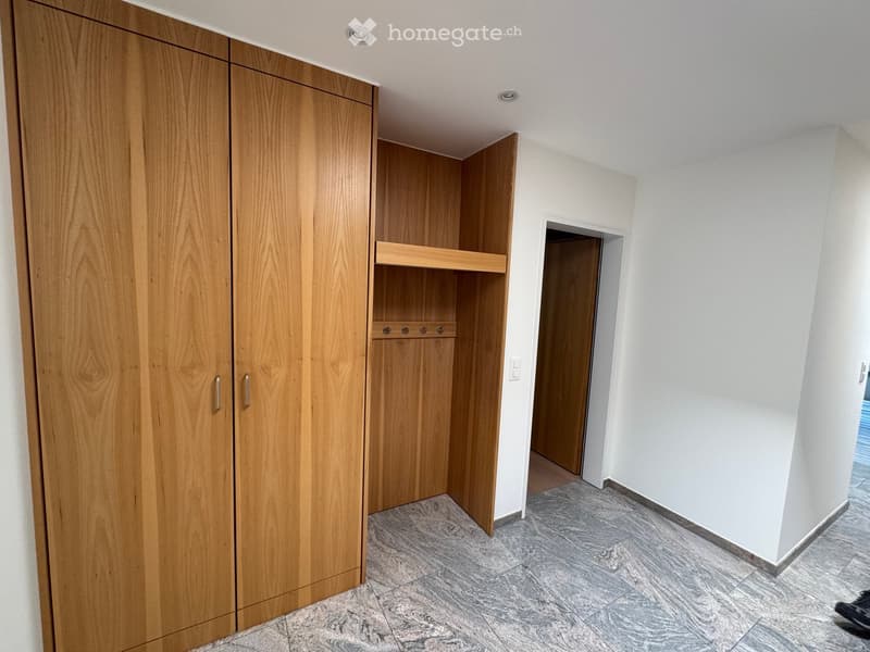 Empty hallway with light wooden built-in closet, tiled floor, and white walls.